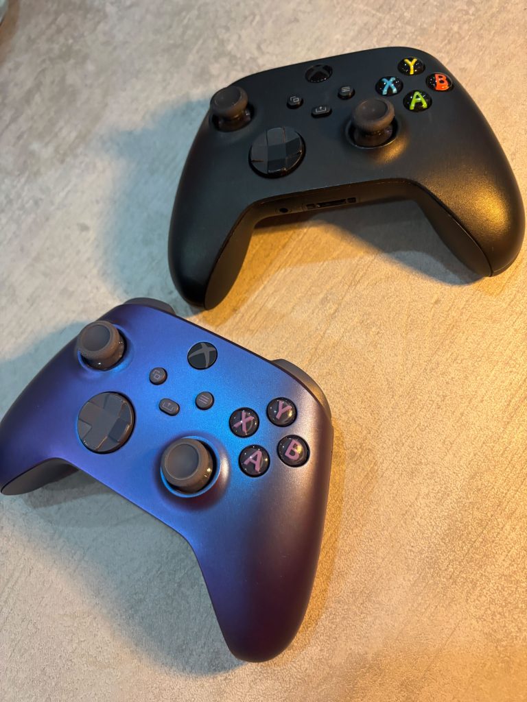 Due controller Xbox, uno nero e uno blu, appoggiati su una superficie chiara