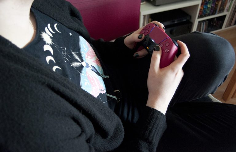 Una persona seduta impugna un controller PlayStation 5 rosa
